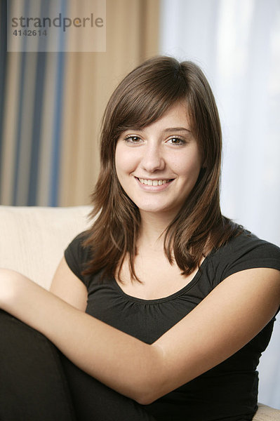 17-jähriges Mädchen sitzt auf Sofa und lächelt