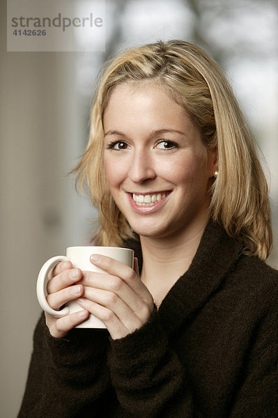 Junge Frau im dunklen Pullover lächelt  mit Tasse