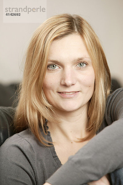 Blonde Frau auf braunem Sofa lächelt  Portrait