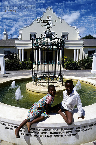 Zwei fröhliche farbige Kinder am Brunnen vor dem Rathaus in Franschhoek bei Stellenbosch  Kapprovinz  Western Cape  Südafrika  Afrika