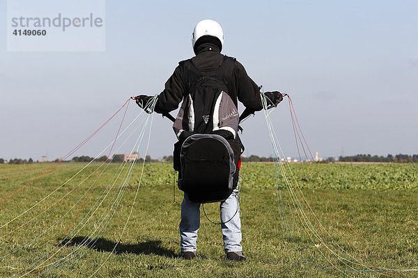 Gleitschirmflieger auf einem Feld in Startposition  hält die Fäden in der Hand  NRW  Deutschland