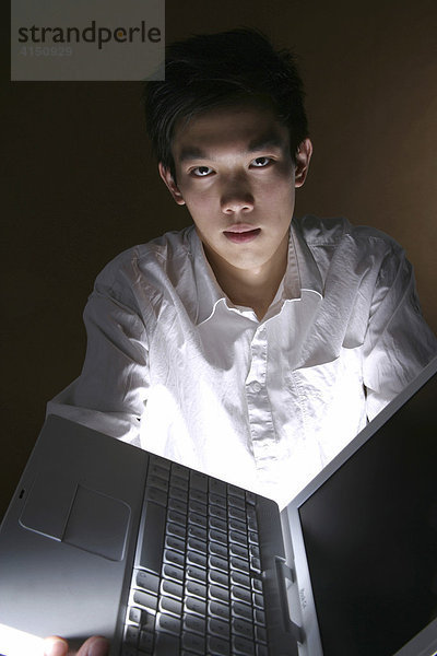 Junger Mann hält Laptop mit ausgestreckten Armen