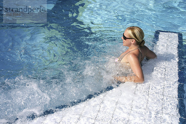 Junge Frau lehnt am Beckenrand eines Schwimmbades