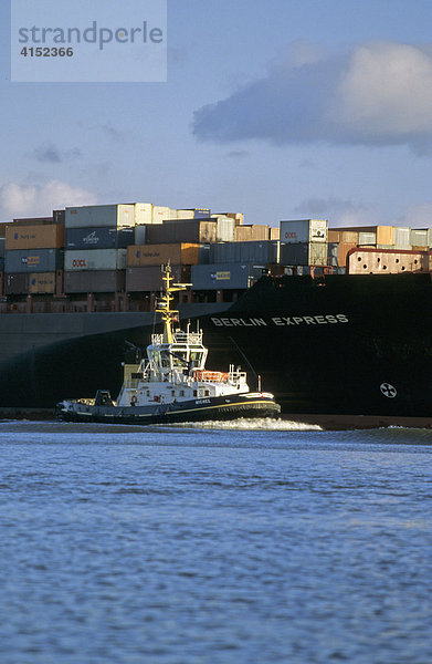 Ein Schlepper begleitet ein großes Containerschiff auf der Elbe bei Hamburg