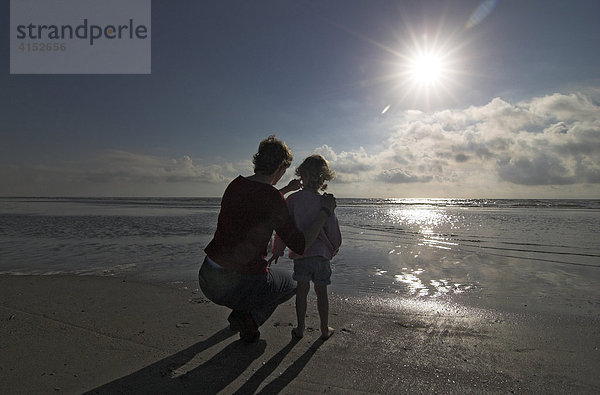 Junge Frau und ihre kleine Tochter hocken am Strand und schauen auf das Meer  Dänemark
