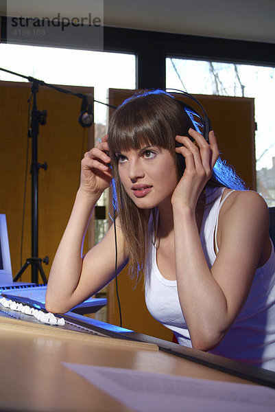 Konzentrierte junge Frau hört mit Kopfhörer am Mischpult eines Tonstudios