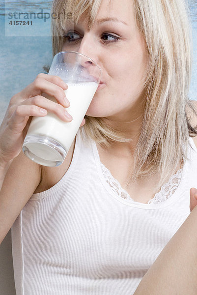 Blonde Frau in Unterwäsche frühstückt im Bett und trinkt ein Glas Milch