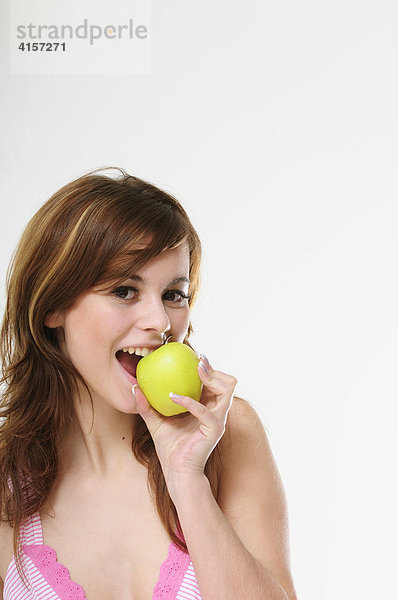 Hübsche junge braunhaarige Frau isst einen grünen Apfel