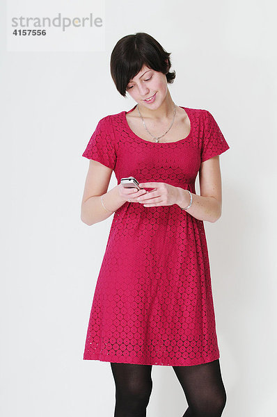 Schwarzhaarige Frau vor weißem Hintergrund blickt auf Handy und lacht