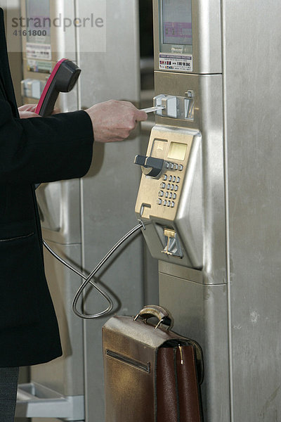 Eine Person zahlt ihr Telefongespräch an einem öffentlichen Telefon der Deutschen Telekom