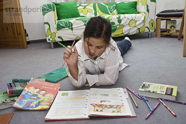 Junge Schülerin liest in einem Buch im Kinderzimmer auf dem Boden