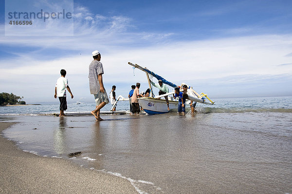 Fischerboot - Auslegerboot ist vom Fischfang zurückgekommen und wird von Fischern an den Strand gezogen  Senggigi  Insel Lombok  Kleine-Sunda-Inseln  Indonesien