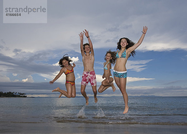 Vier Kinder springen vor Freude am Strand in die Luft  Insel Lombok  Kleine Sunda-Inseln  Indonesien  Asien