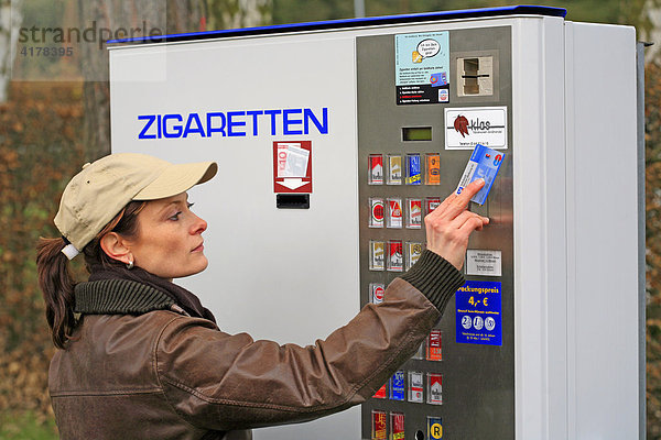 Eine junge Frau holt Zigaretten am Zigarettenautomat. In der rechten Hand hält sie eine EC-Karte zur Alterskennung die in den Automat eingesteckt wird.