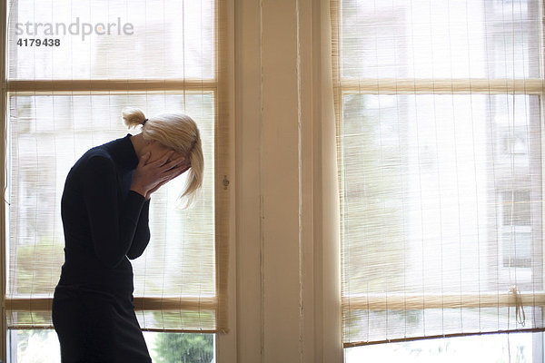 Traurige blonde Frau vor großen Fenstern