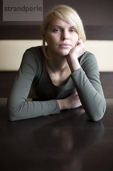 Blonde Frau sitzt traurig in einer Bar an einem Tisch