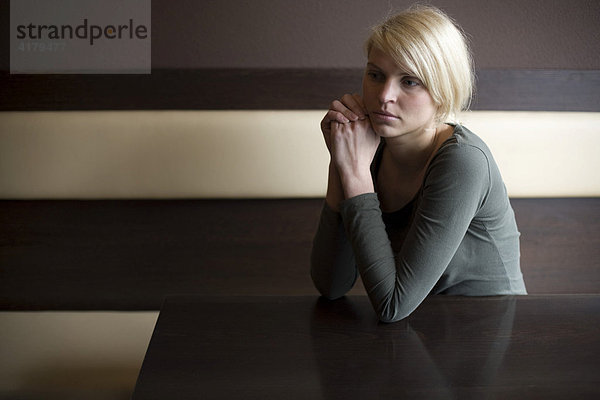Blonde Frau sitzt einsam an einem Tisch in einer Bar