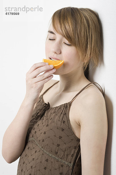 Junge Frau lehnt an einer Wand und ißt ein Stück Orange