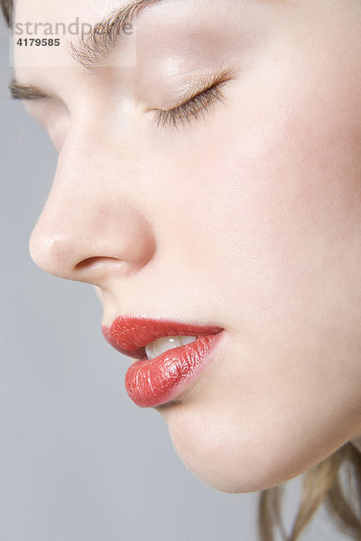 Nahaufnahme des Gesichts einer jungen Frau mit roten Lippen und geschlossenen Augen im Profil mund