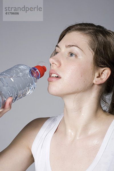 Junge Frau trinkt beim Fitnesstraining aus einer Wasserflasche