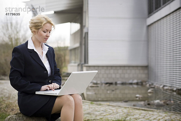 Geschäftsfrau arbeitet vor einem Bürogebäude an einem Notebook