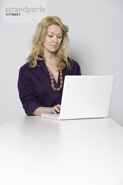 Junge blonde Frau arbeitet an einem Tisch sitzend mit einem weißen Notebook