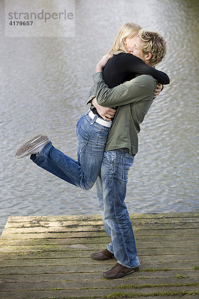 Mann hebt Frau auf einem Holzsteg am Wasser hoch