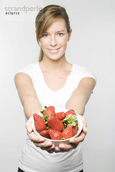 Junge Frau mit langen dunkelblonden Haaren hält lächelnd eine Schale Erdbeeren