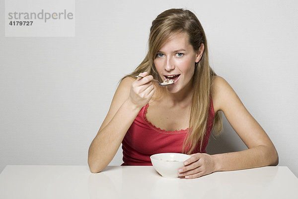 Junge Frau sitzt am Tisch und ißt Müsli