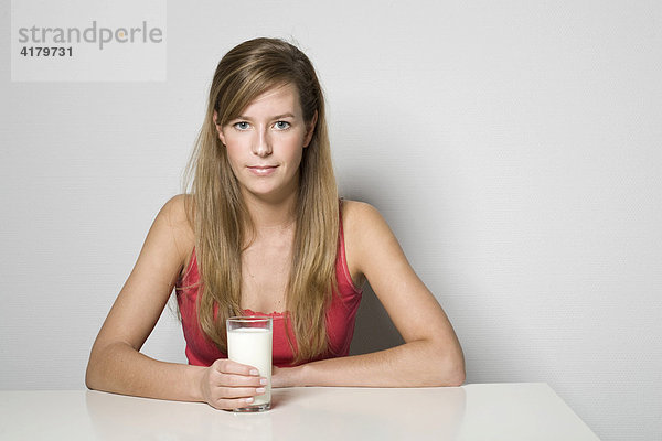 Junge Frau sitzt an einem Tisch und hält ein Glas Milch in der Hand