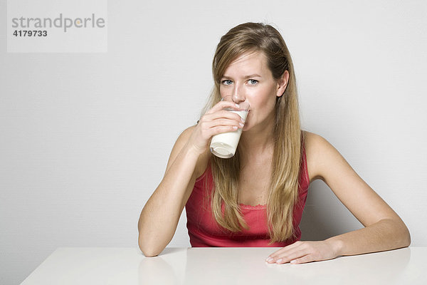 Junge Frau sitzt an einem Tisch und trinkt ein Glas Milch
