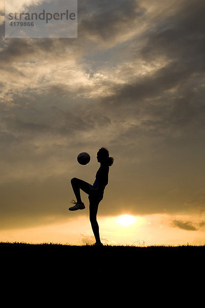 Silhouette einer jungen Frau beim Fußballspielen vor abendlichem Himmel
