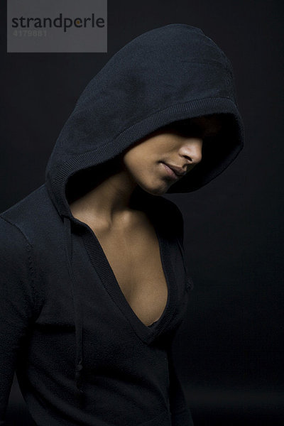 Dunkelhäutige Frau mit Kapuze über dem Kopf vor Schwarz