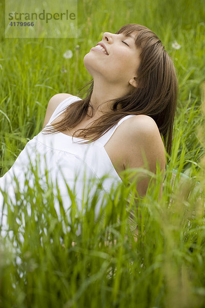 Junge dunkelhaarige Frau in einem weißen Kleid liegt entspannt auf einer Wiese  genießt den Sommer