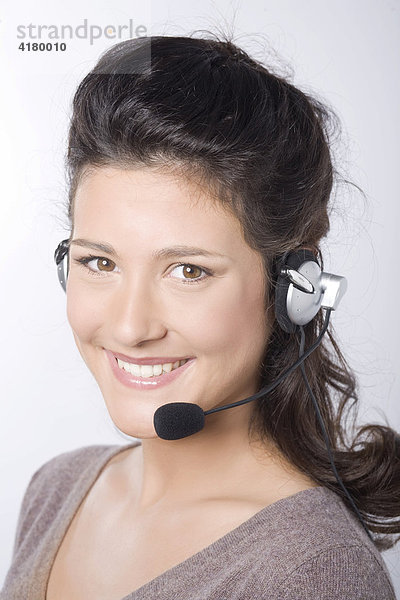 Junge dunkelhaarige Frau lacht beim Telefonieren mit Headset