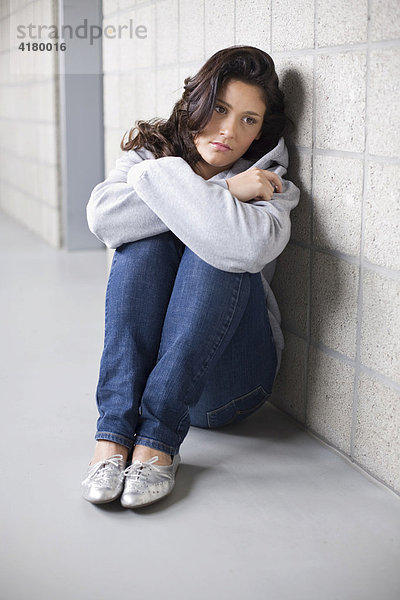 Junge Frau sitzt traurig auf dem Boden und lehnt an einer Wand