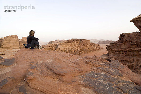 Frau sitzt auf Felsvorsprung und blickt in die Ferne  Wadi Rum  Jordanien  Naher Osten
