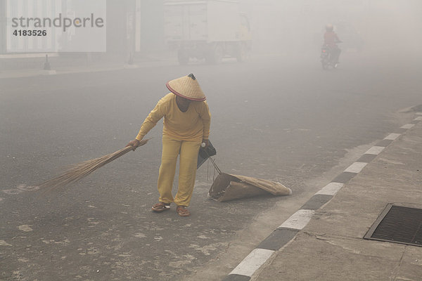 Frau kehrt Straße im Smog von Pangkalanbun  Zentral-Kalimantan  Borneo  Indonesien