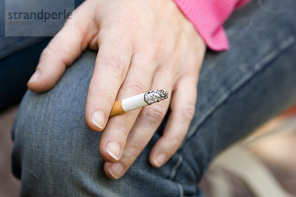 Eine Frauenhand mit einer brennenden Zigarette - Querformat