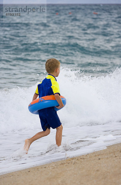 Ein Junge  5 Jahre  mit Schwimmreifen und Neoprenanzug  rennt am Strand  Marina di Orosei  Sardinien  Italien