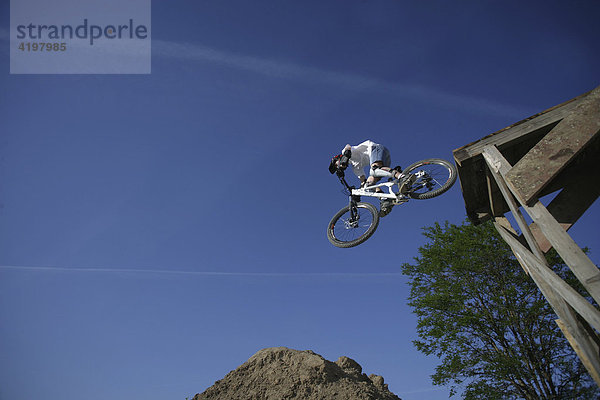 Ein jugendlicher springt mit seinem Mountainbike von einer Rampe.