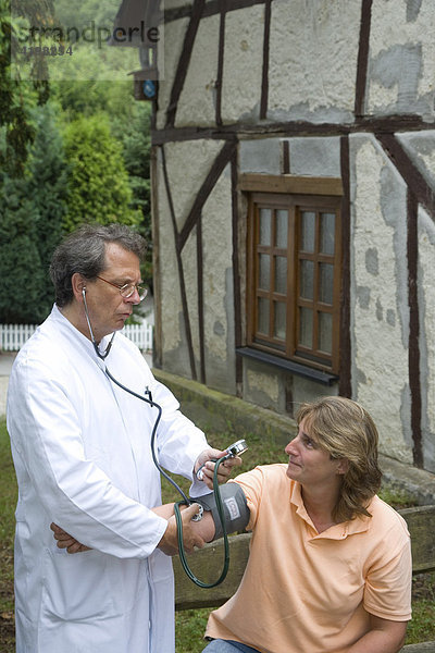 Ein Landarzt misst seiner Patientin bei einem Hausbesuch den Blutdruck