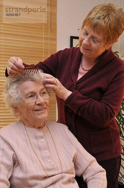 Pflegerin kämmt pflegebedürftiger Seniorin die Haare