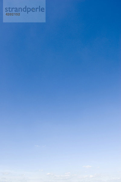 Ein leerer dunkelblauer Himmel bei schönem Wetter geht zum Horizont hin in weiß über und zeigt dort ein paar kleine Wolken