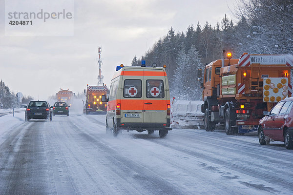 Notarztwagen und Winterdienst Streufahrzeug Räumfahrzeug Schneepflug Kolonne auf Autobahn Bayern Deutschland