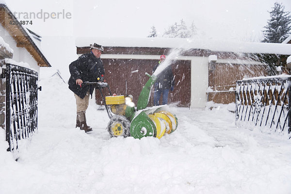 Hauseigentümer beim Schneeräumen mit Schneefräse in Schneetreiben Bayern Deutschland