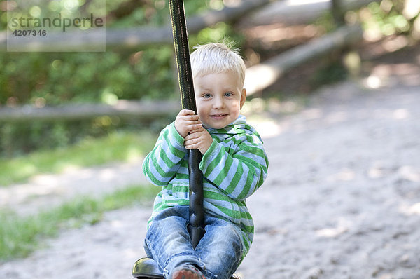 Blonder Junge sitzt auf einer Seilschaukel