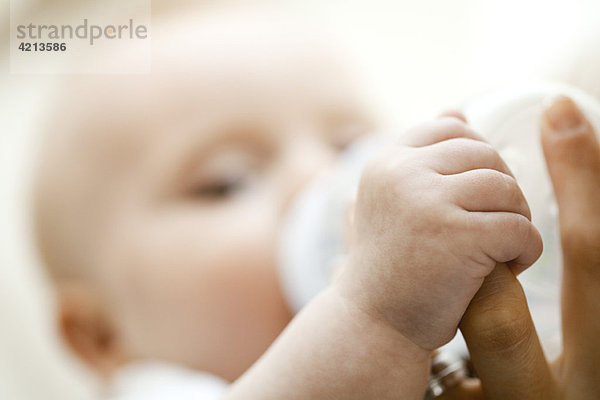 Baby trinkt aus der Flasche und hält den Finger der Mutter  Nahaufnahme