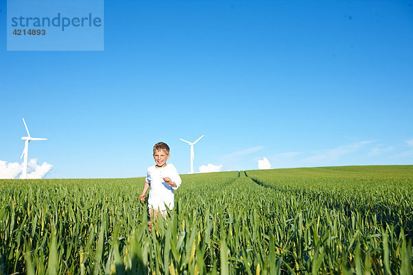 Junge läuft auf dem Feld mit Windkraftanlagen
