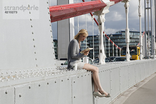 Frau sitzt auf der Brücke und schaut sich das Buch an.